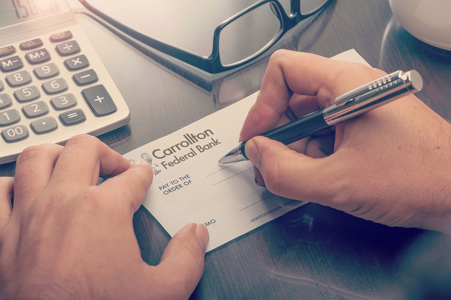 Customer filling out a check with the Carrollton Federal Bank Logo on it