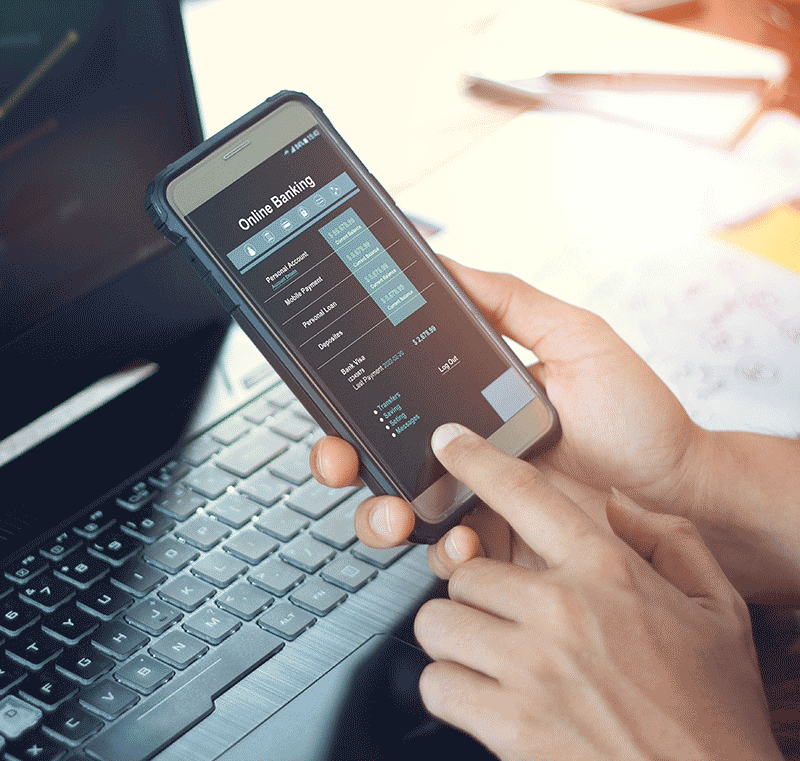 Hand using mobile banking on a cell phone in front of a computer